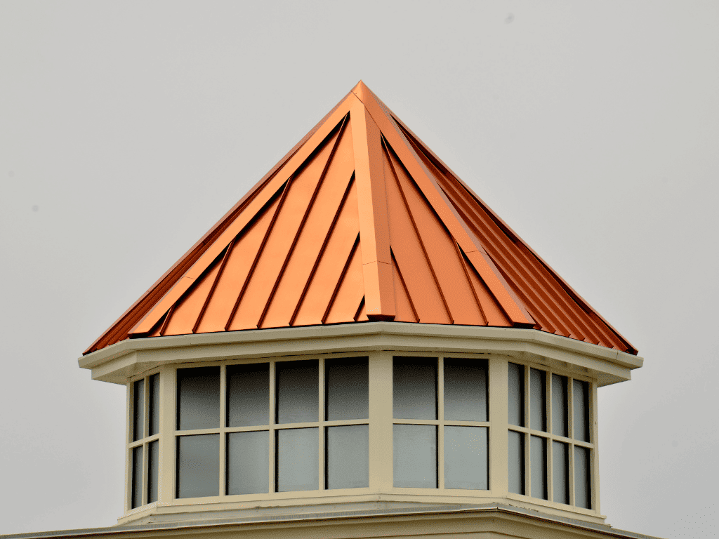 Copper-colored standing seam metal roof atop an octagonal tower with windows, against a gray overcast sky.