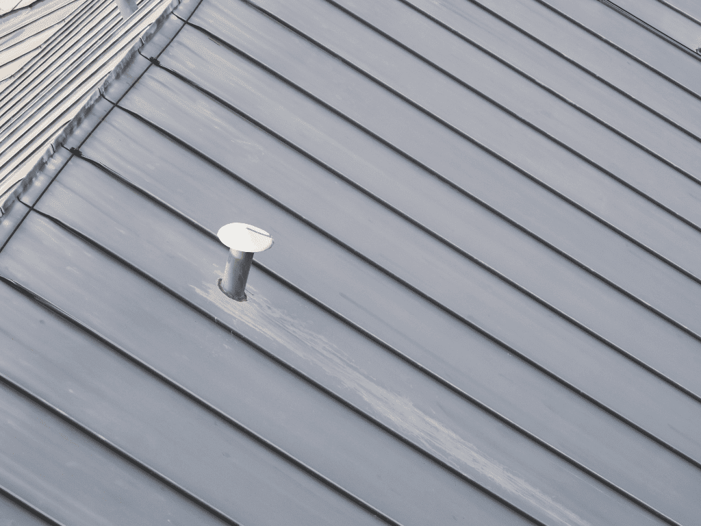 Overhead view of a gray standing seam metal roof with a single roof vent, showing clean alignment and matte finish.